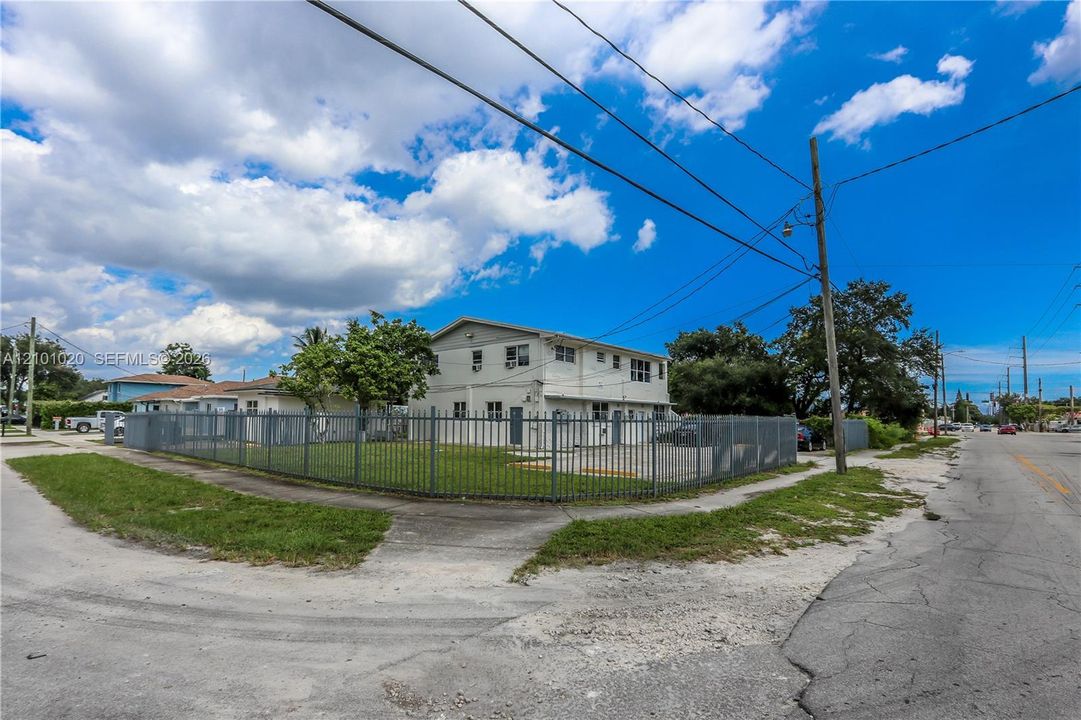 Two-story multi-unit structure featuring a corner lot location, exterior metal fencing, and a manicured lawn