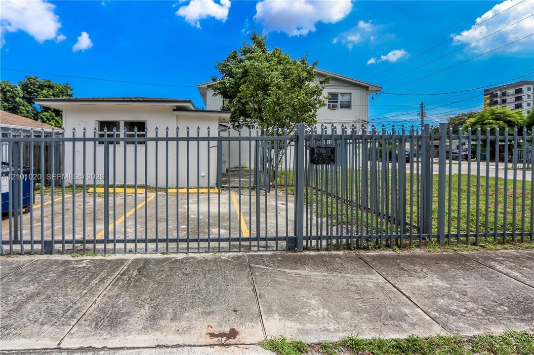 Multi-story exterior featuring a concrete parking area, metal perimeter fencing, and dual-level structural design