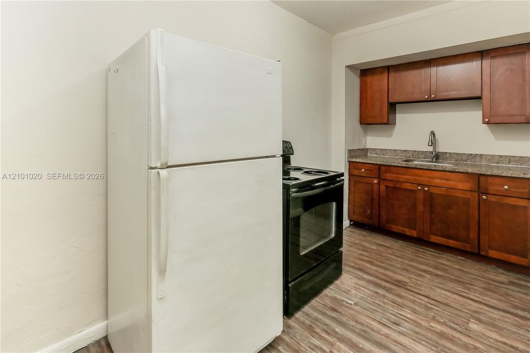 Kitchen featuring medium-tone wood cabinetry, stone-finish countertops, stainless steel sink with high-arch faucet, black electric range, and white refrigerator