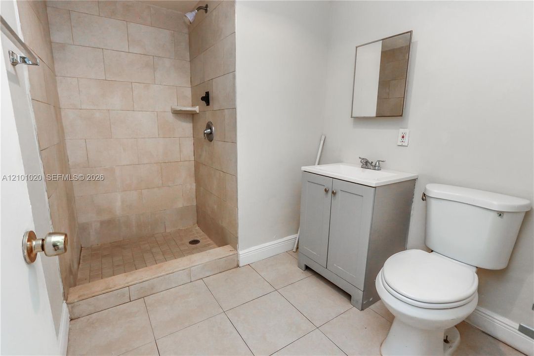 Walk-in shower with large-format stone-finish tile surround, grey vanity cabinet, white countertop, and wall-mounted mirror