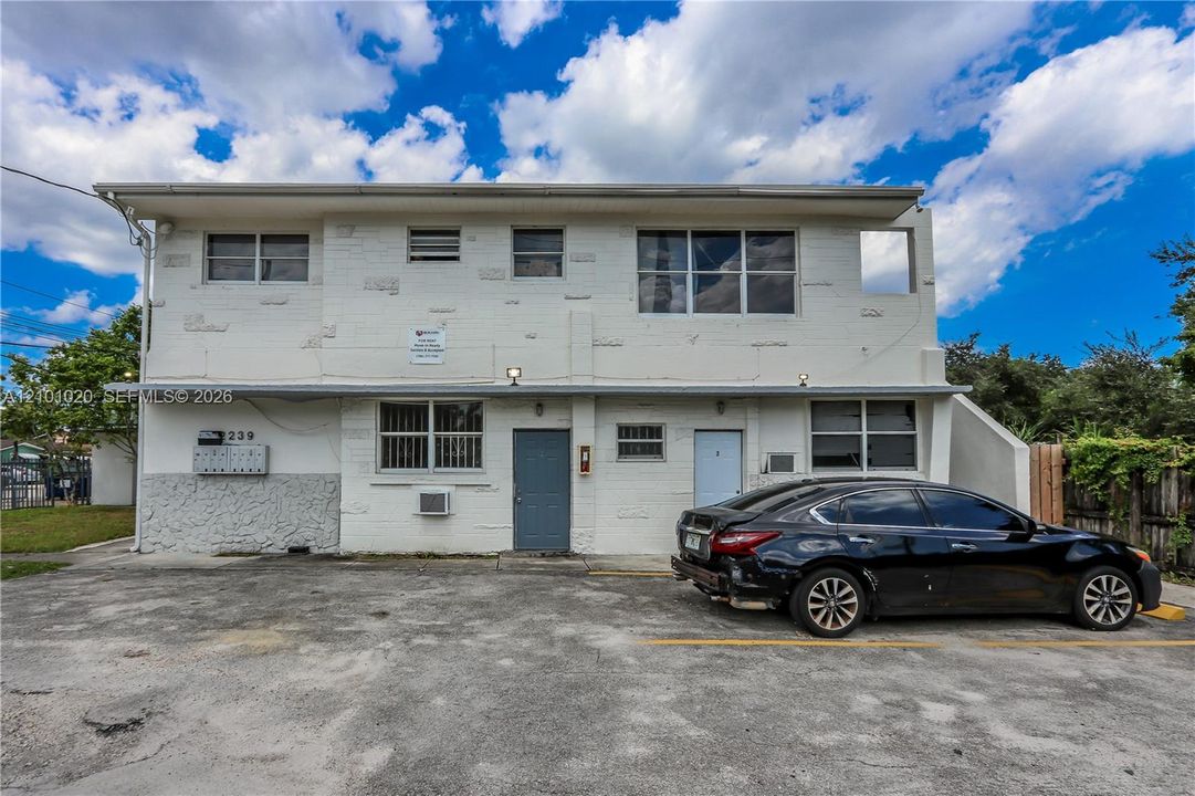 Two-story multi-unit structure featuring a painted masonry exterior, concrete paved parking area, and multi-unit wall-mounted mailbox system