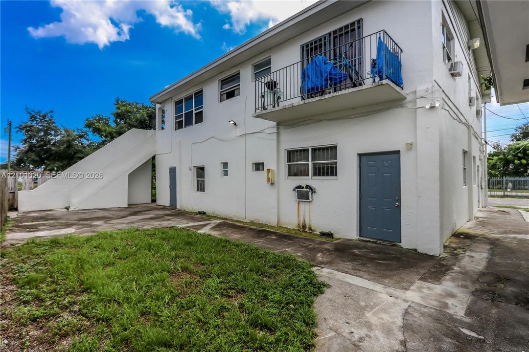 Exterior elevation featuring a stucco finish, an elevated metal balcony with railing, concrete staircase, and paved ground level area