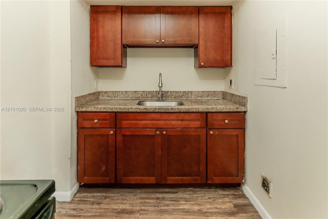 Wood-finish cabinetry featuring upper and lower storage, stone-finish countertop, stainless steel sink, and high-arc faucet