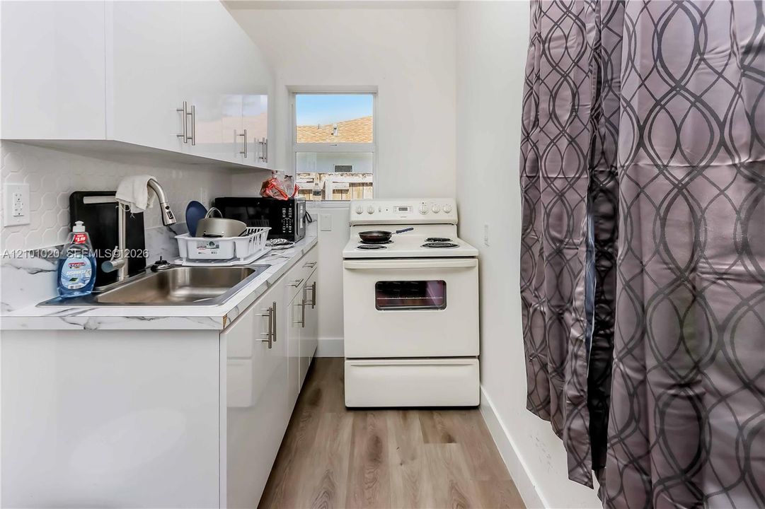 Kitchen featuring high-gloss white cabinetry, stone-patterned countertops, stainless steel sink with a gooseneck faucet, white electric range, and wood-finish flooring