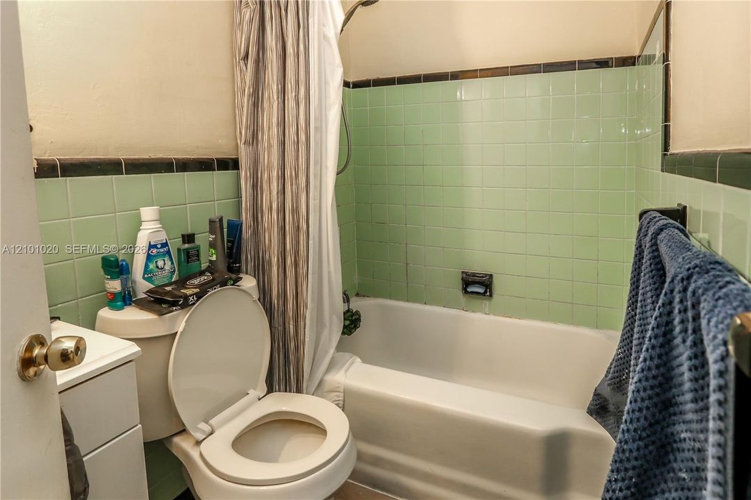 Full-size bathtub featuring light green wall tiling with a dark trim border, integrated soap niche, and polished metal plumbing fixtures