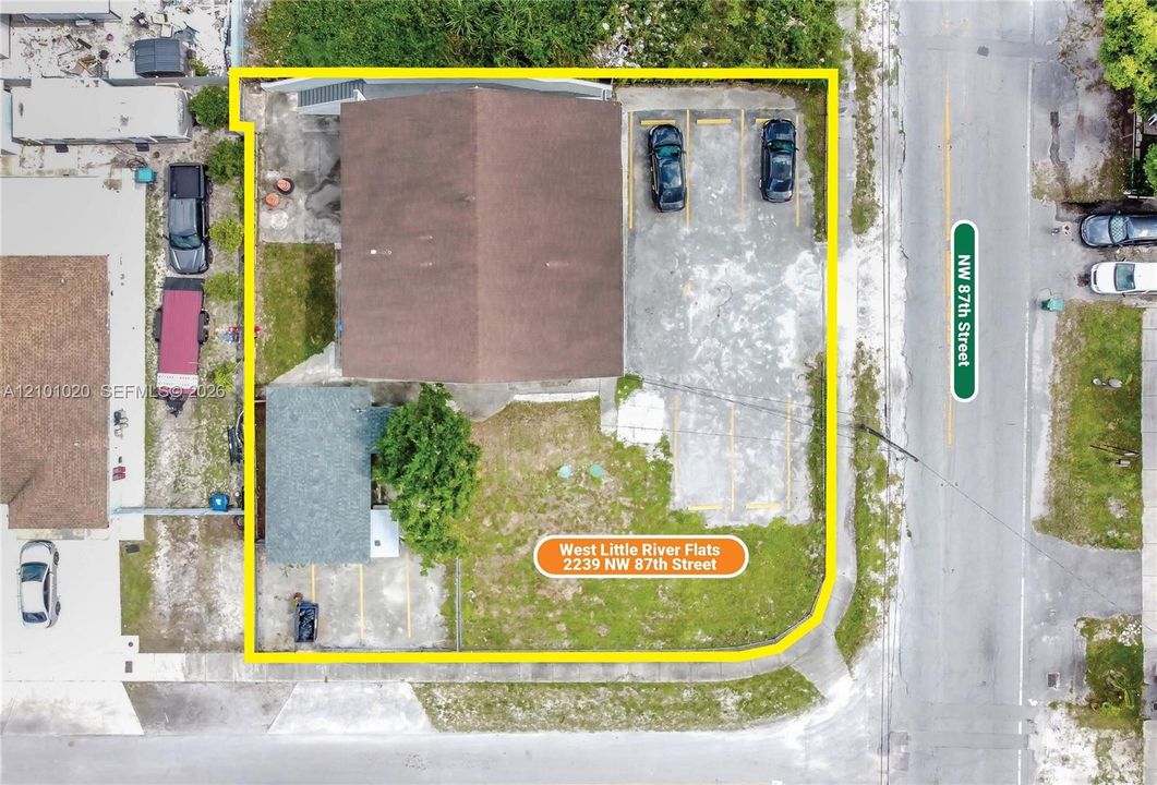 Aerial perspective of a property lot featuring an asphalt-paved surface parking area with marked stalls and a rectangular building footprint