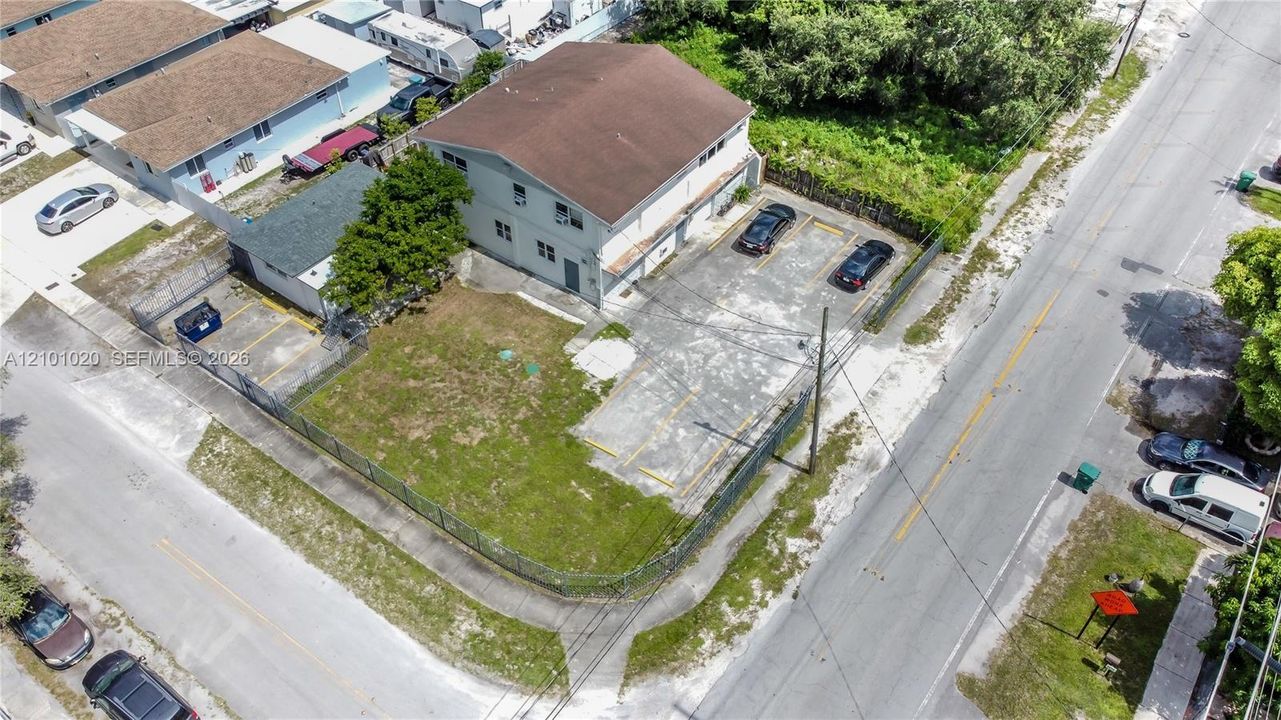 Multi-story structure featuring a pitched roof, exterior cladding, a paved parking area with marked spaces, and a chain-link fenced perimeter