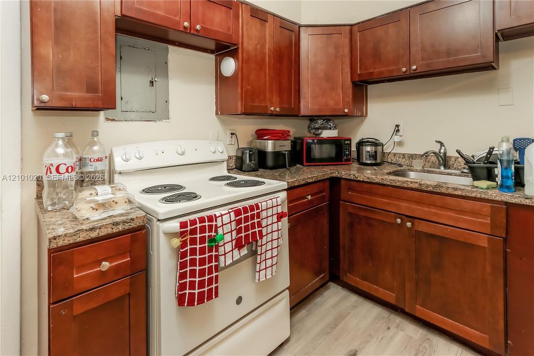Kitchen featuring stained wood cabinetry, stone-patterned countertops, a stainless steel sink with a high-arch faucet, a white electric range, and wood-finish flooring