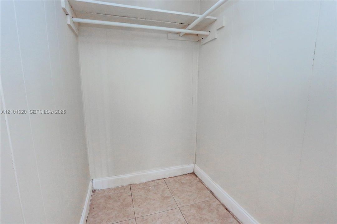 Storage area featuring white paneling, ceramic tile flooring, and a built-in horizontal shelf with a hanging rod