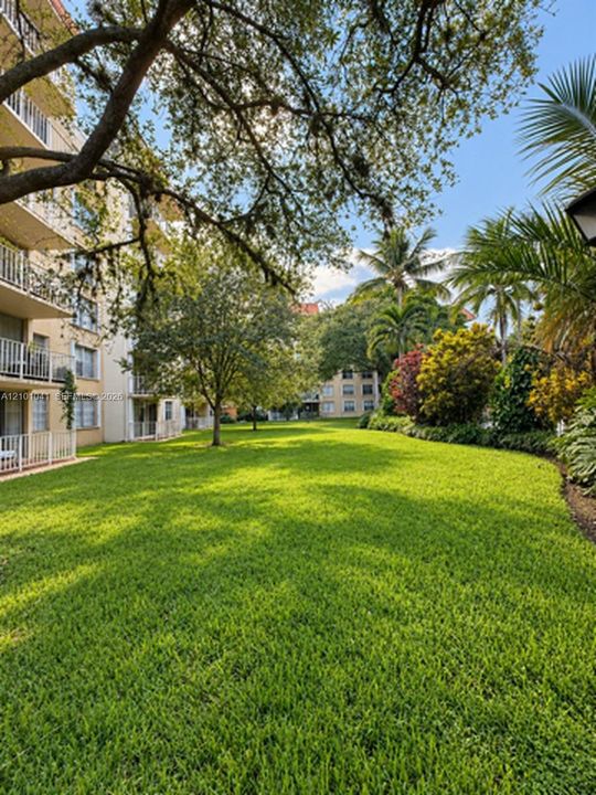 Expansive grounds featuring a manicured lawn, mature trees, assorted tropical landscaping, and structural balconies