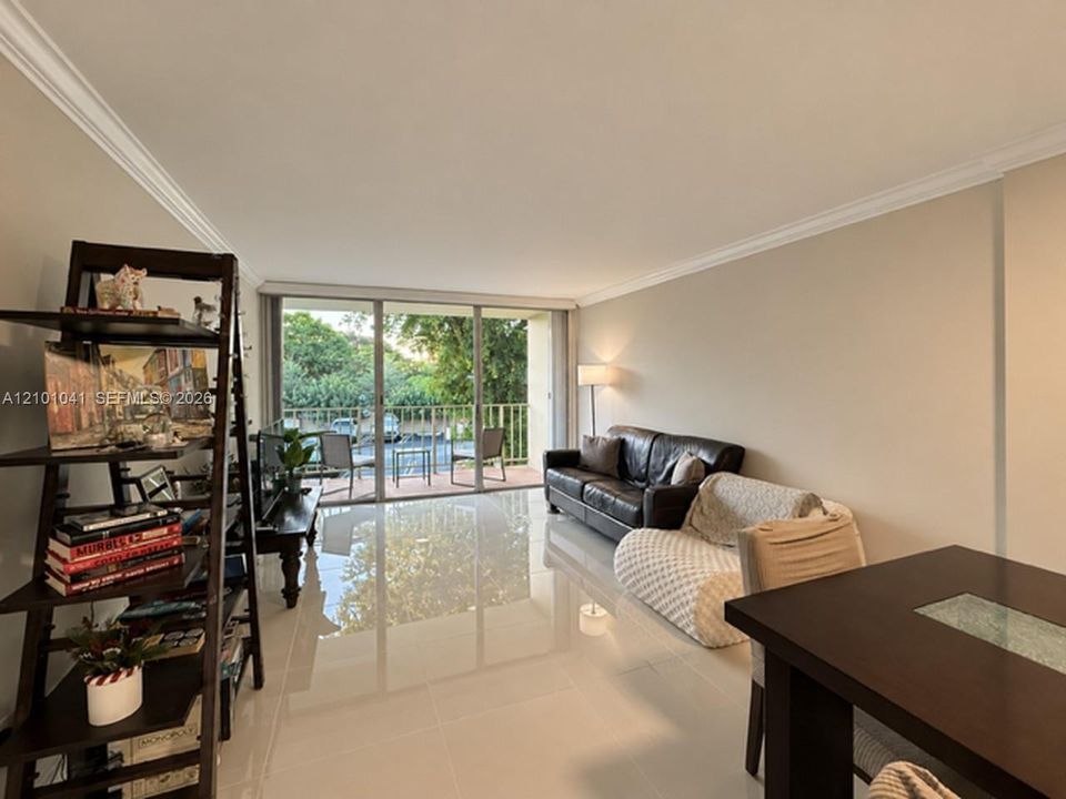 Living area featuring large-format tile flooring, crown molding, and floor-to-ceiling sliding glass doors opening to a private balcony