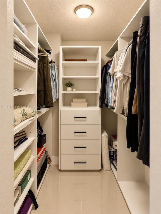 Walk-in closet featuring white built-in shelving, four-drawer cabinetry with matte black pulls, and tile flooring