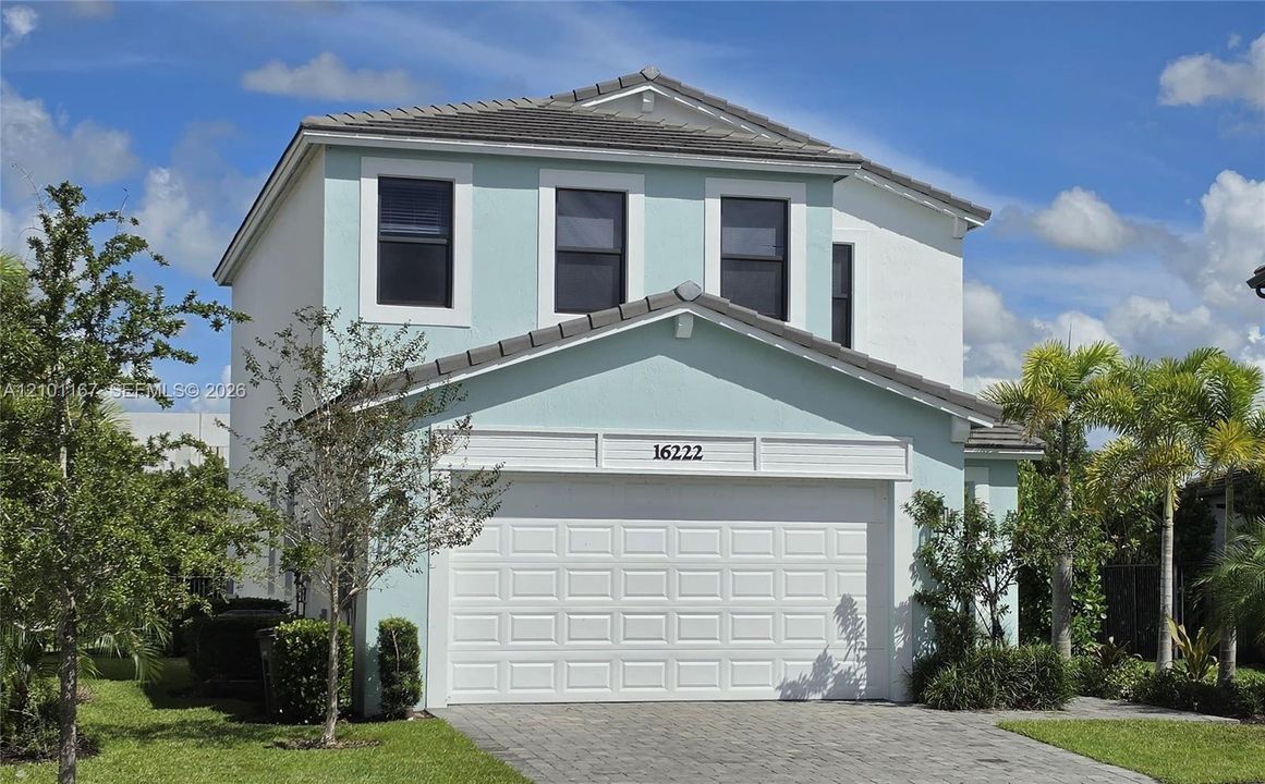 Two-story exterior featuring light-toned stucco siding, a tiled roof, a multi-panel garage door, and a paved driveway