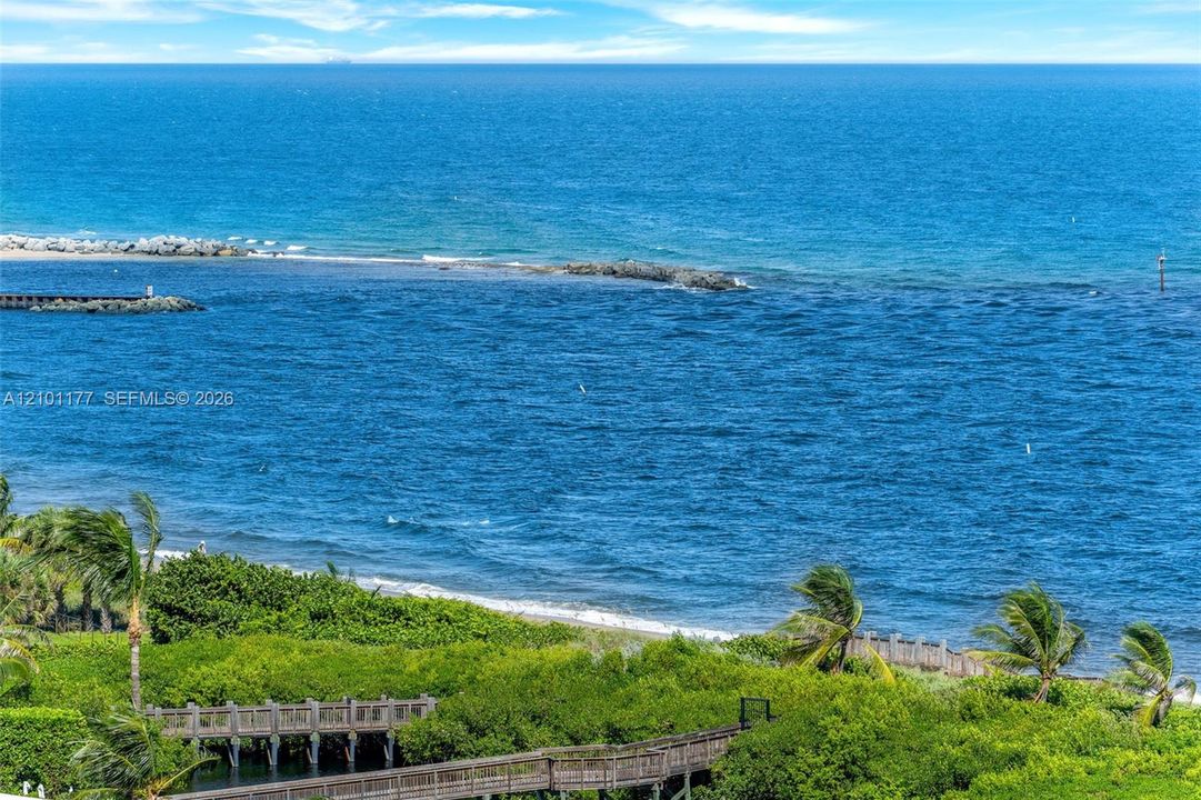 Direct oceanfront exposure featuring a coastal jetty, sandy shoreline, lush greenery, and a wooden pedestrian walkway