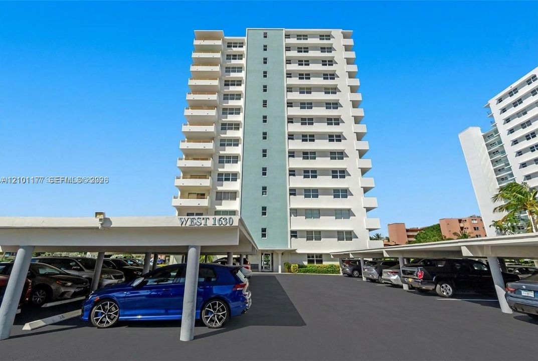 High-rise residential exterior featuring stacked private balconies, a central vertical accent wall, and covered parking structures