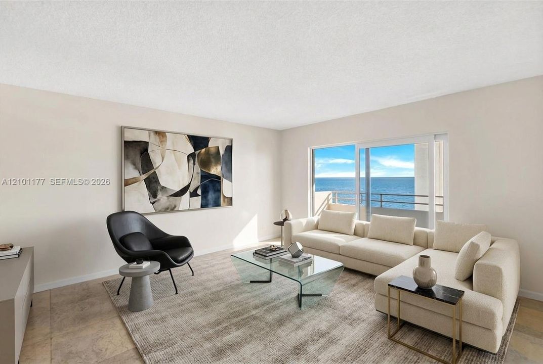 Living area featuring stone tile flooring, neutral walls, and a large sliding glass door opening to a private balcony with ocean scenery