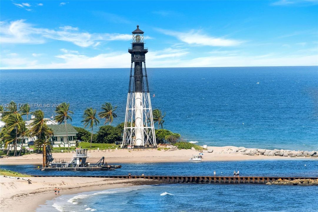 Lighthouse exterior featuring a tapered metal-lattice structure, open-air gallery, and glass-enclosed lantern room situated on a coastal sand beach
