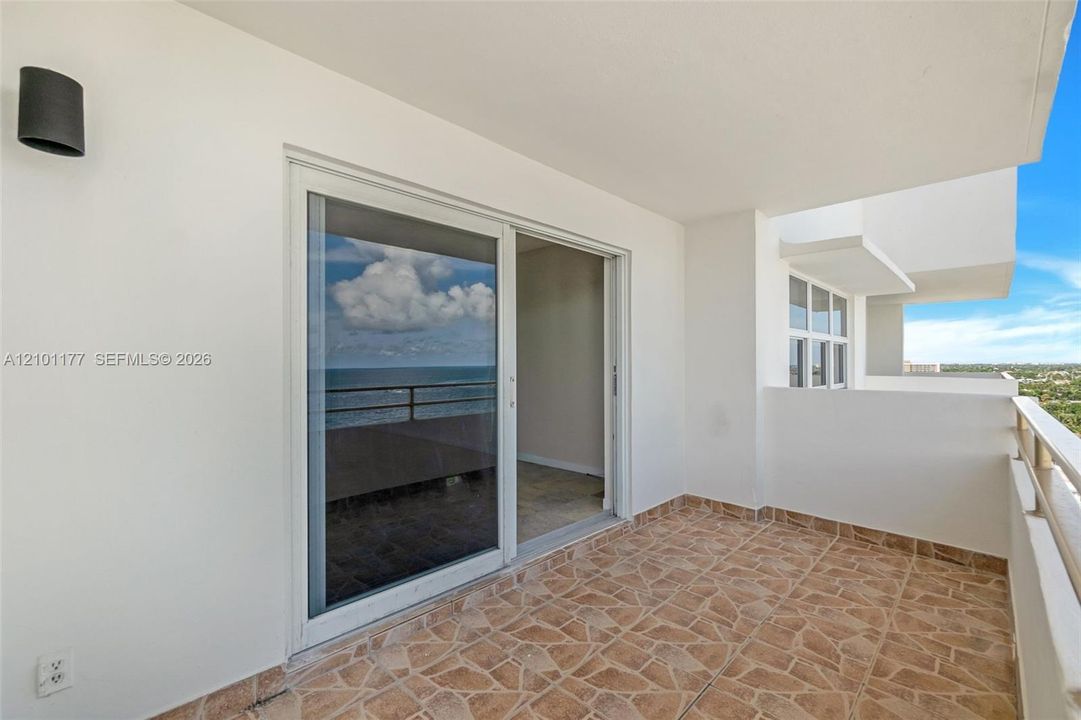 Covered balcony featuring stone-tile flooring, glass sliding doors, wall-mounted exterior lighting, and a metal railing