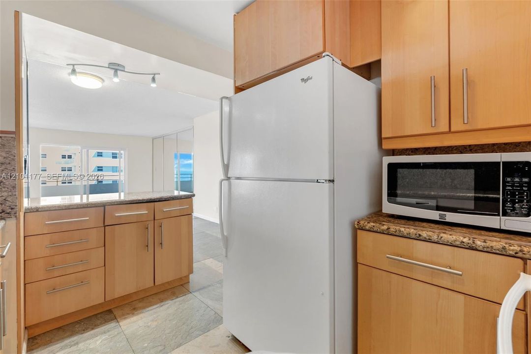 Kitchen featuring light-finish cabinetry, stone-texture countertops, tile flooring, and integrated built-in microwave