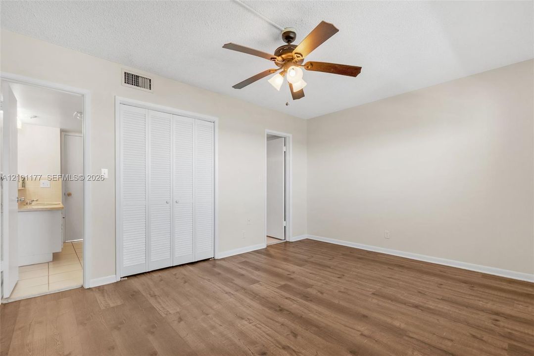 Room featuring wood-finish flooring, a ceiling fan with light fixture, and floor-to-ceiling louvered bi-fold closet doors