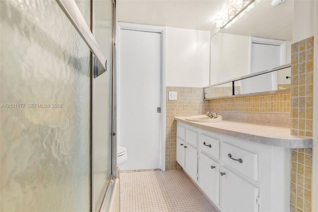 Bathroom featuring white cabinetry, a single-basin vanity, tiled backsplash, large wall-mounted mirror, and a glass-enclosed shower