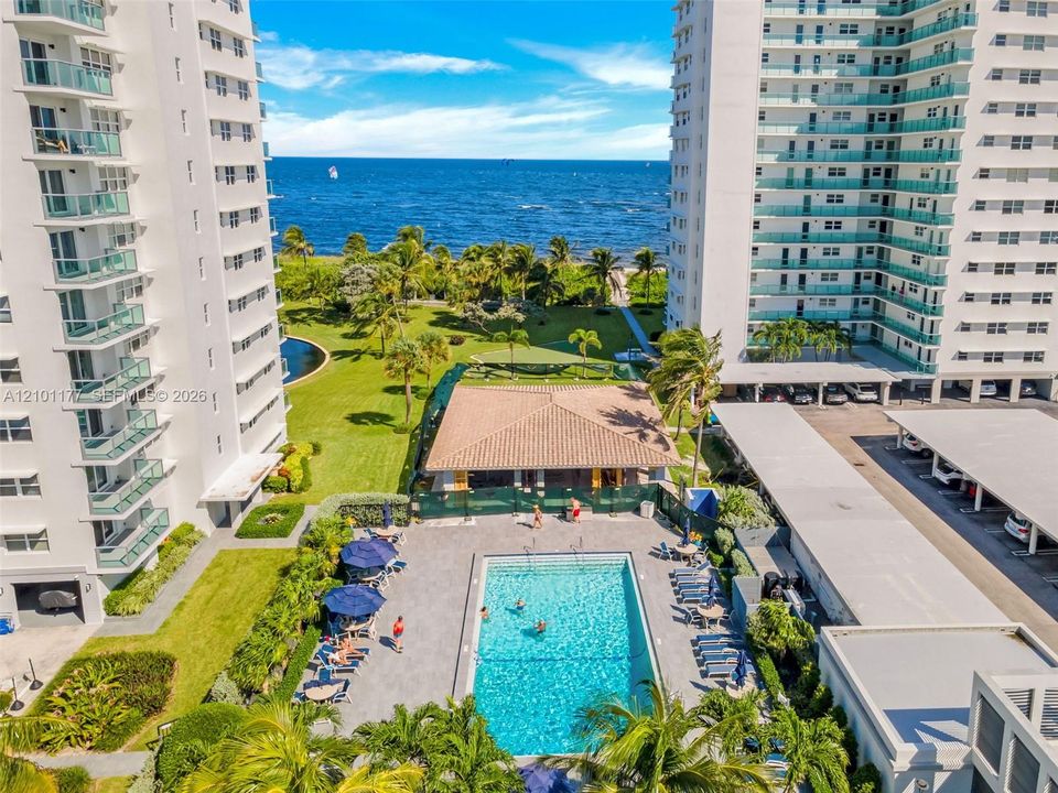 High-rise residential complex featuring a swimming pool, covered pavilion, manicured grounds, and oceanfront placement