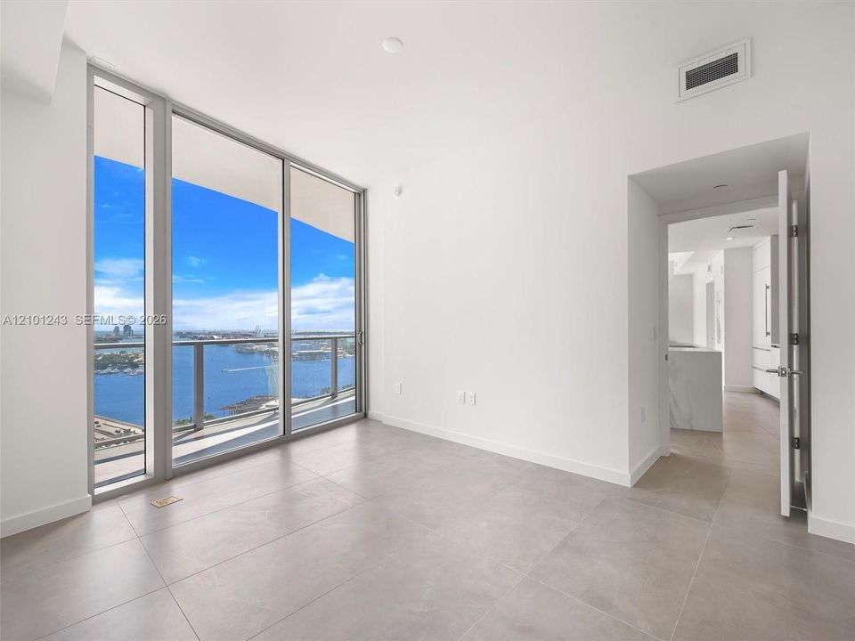 Floor-to-ceiling glass windows, private balcony, neutral tile flooring, and metal-framed sliding glass doors