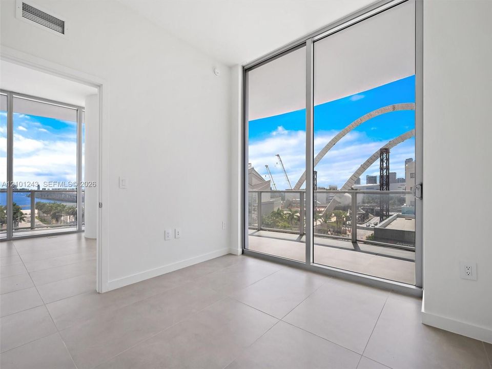Floor-to-ceiling sliding glass doors, private balcony with metal railing, large-format tile flooring, and neutral wall finishes