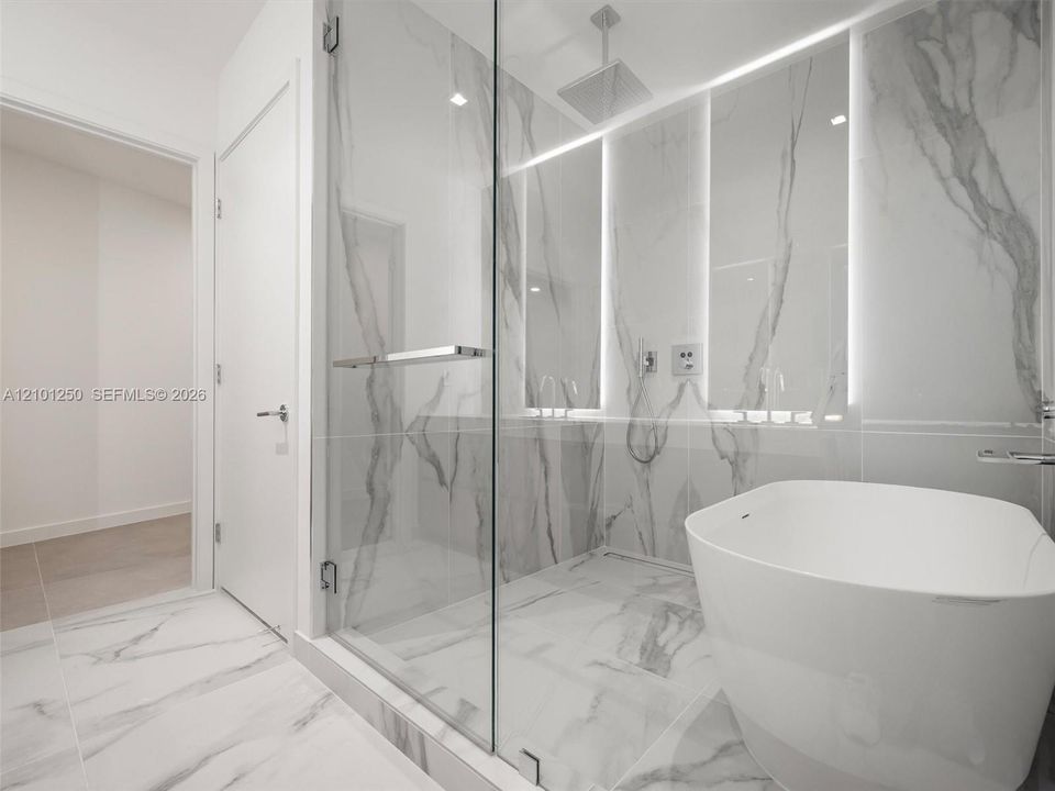 Glass-enclosed shower with large-format veined tile, integrated wall lighting, overhead rain shower head, and freestanding white soaking tub