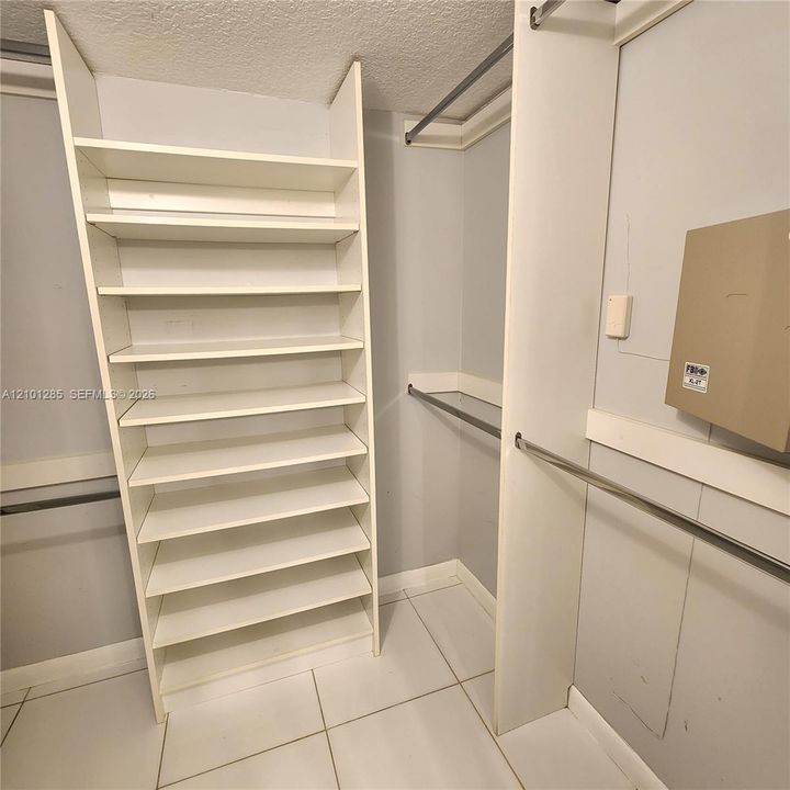 Custom walk-in storage featuring multi-level white shelving, horizontal metal hanging rods, and tile flooring