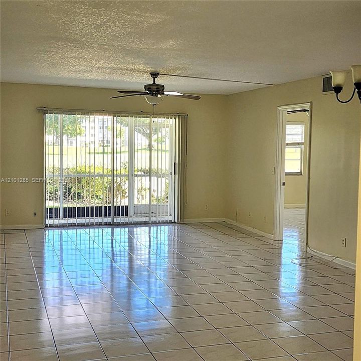 Interior space featuring light-toned ceramic tile flooring, sliding glass doors with vertical blinds, a ceiling fan, and a neutral wall finish