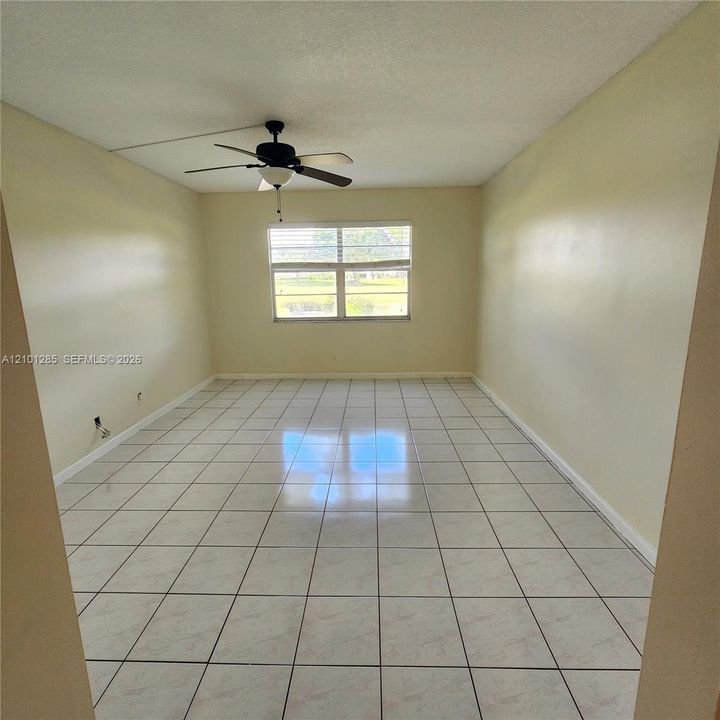 Room featuring neutral wall paint, white tile flooring, large horizontal window, and a ceiling fan with integrated lighting
