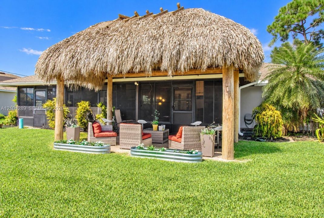 Outdoor living space featuring a thatch-roof palapa, natural wood support beams, metal planter boxes, and a screened enclosure