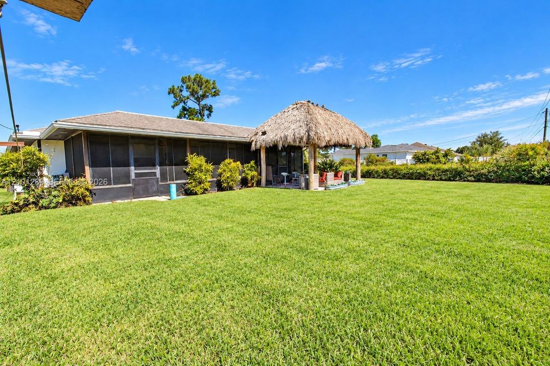 Expansive backyard featuring a manicured lawn, a screen-enclosed patio, and a thatch-roof palapa