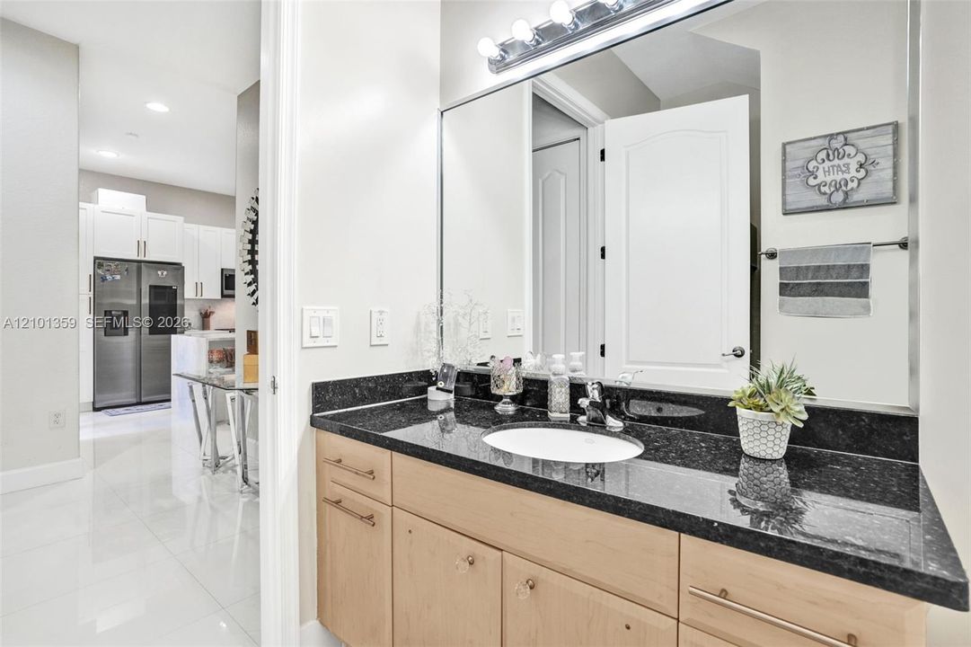 Bathroom vanity featuring dark stone countertops, an integrated undermount sink, light wood-finish cabinetry, a large wall-mounted mirror, and a multi-bulb light fixture