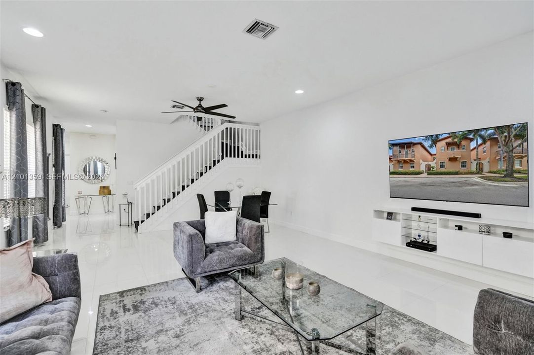 Living area featuring polished tile flooring, recessed lighting, a ceiling fan, a staircase with a white railing, and wall-mounted cabinetry