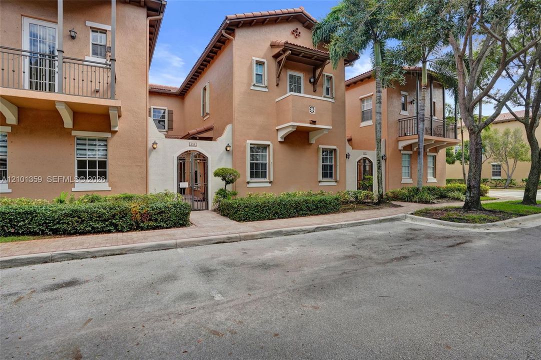 Mediterranean-style stucco exterior featuring terracotta roof tiles, wrought-iron balcony railings, arched gated entryways, and upper-level decorative corbels