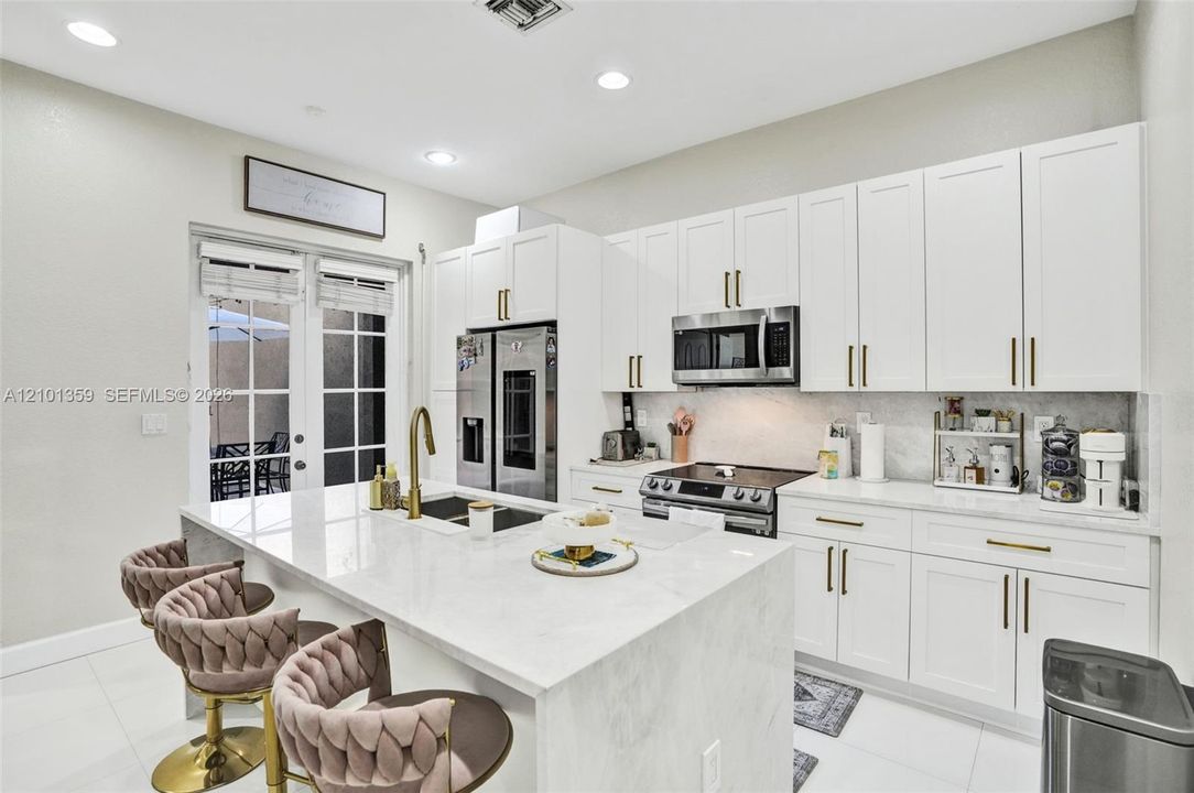 Kitchen featuring white shaker-style cabinetry, quartz countertops with a waterfall-edge island, stainless steel appliances, and gold-finish hardware
