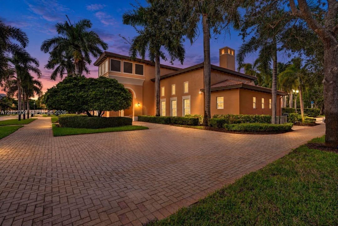 Stucco exterior featuring a paver driveway, multiple vertical windows, a prominent chimney, and mature palm trees