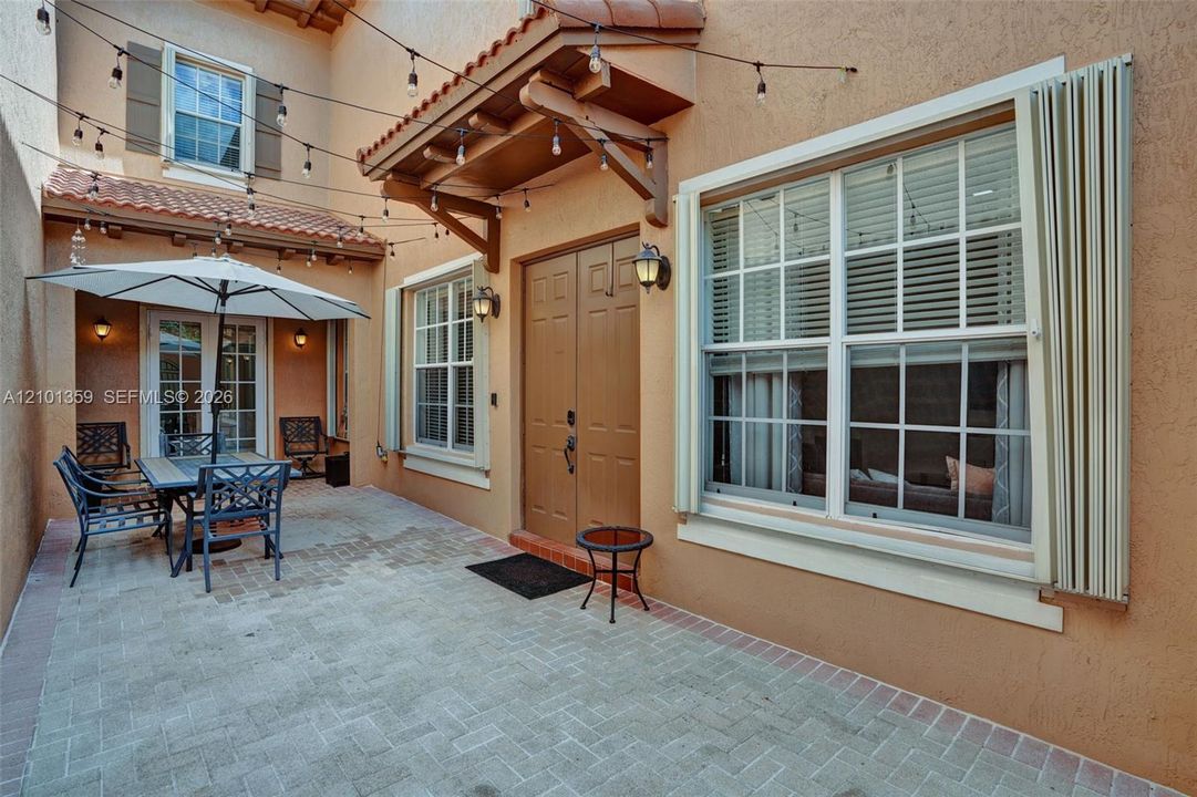 Enclosed courtyard featuring a paved brick patio, double entry doors, wood-accented awning, and exterior wall-mounted light fixtures