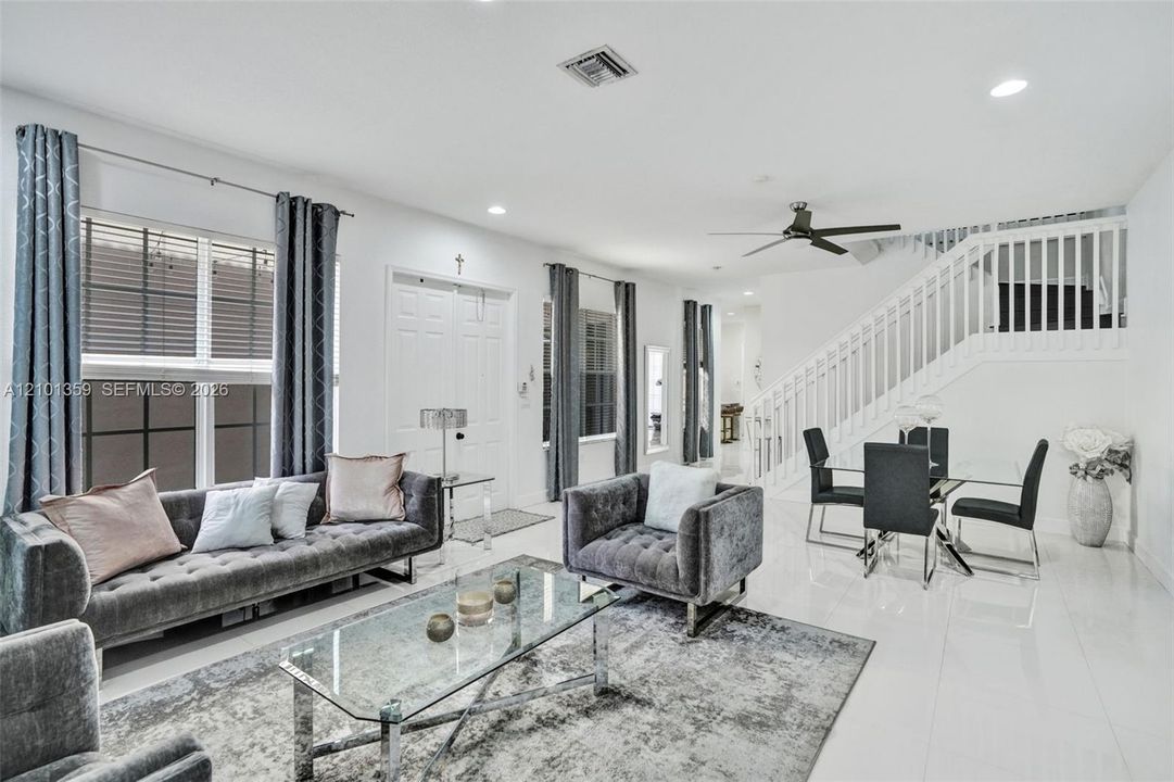 Open-concept living space featuring high-gloss tile flooring, recessed lighting, white stair railing with balusters, and a ceiling fan