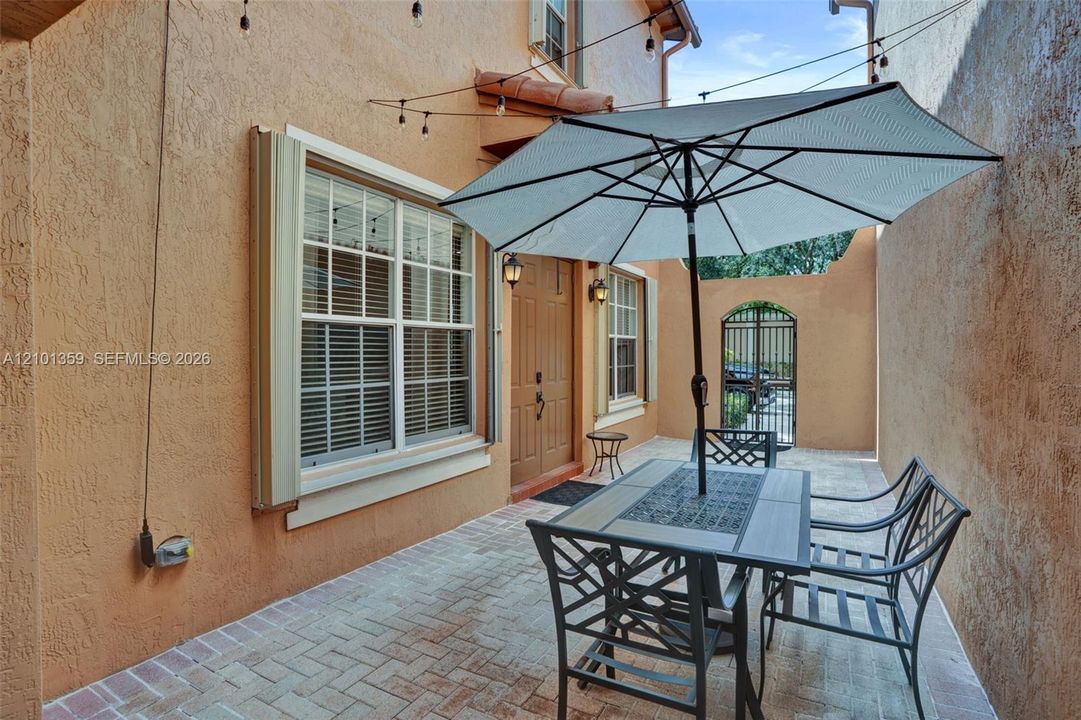 Enclosed courtyard featuring paver flooring, stucco exterior walls, a decorative metal gate, and exterior wall-mounted lanterns