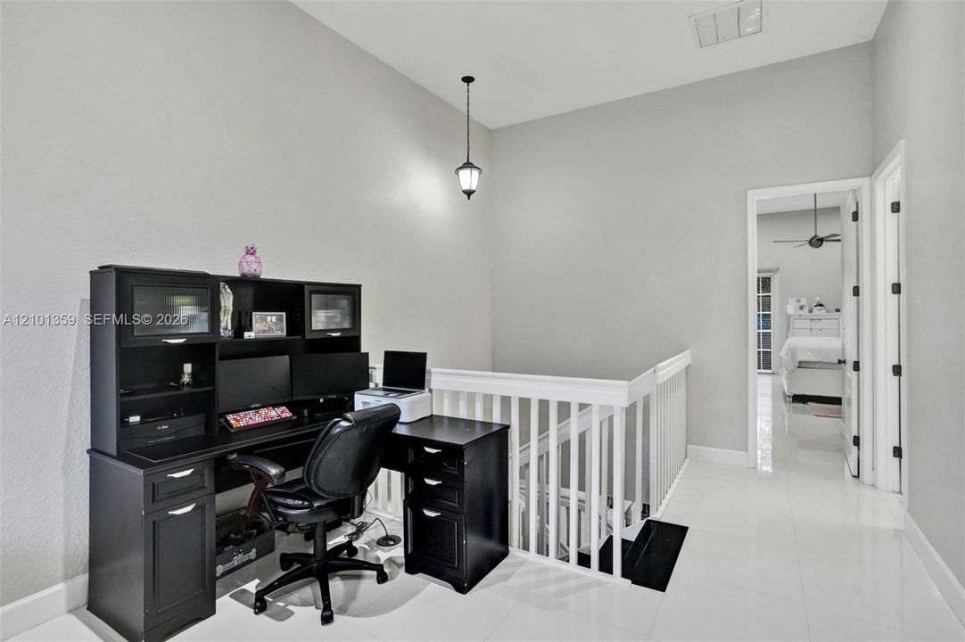 High-ceiling landing featuring glossy tile flooring, a white wooden balustrade, and a hanging pendant light