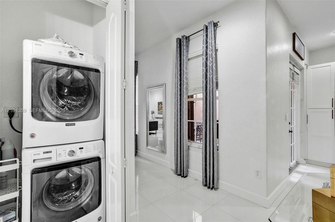 Laundry area featuring stacked front-load appliances, tile flooring, window with blind, and built-in cabinetry