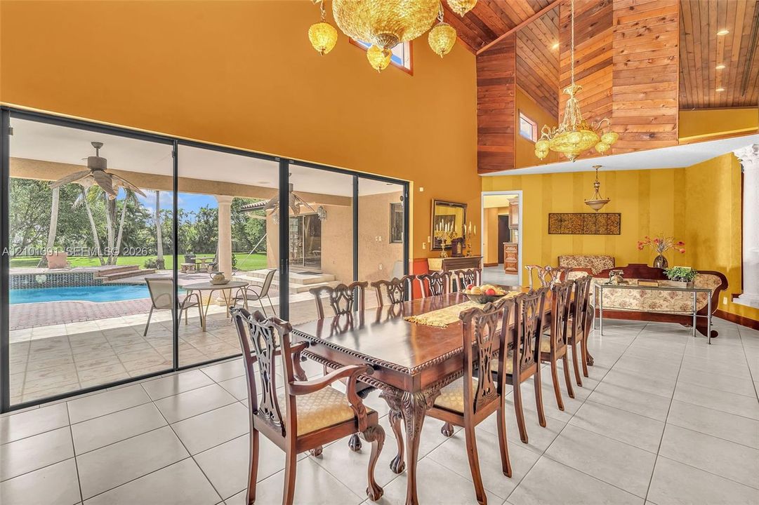Vaulted wood-paneled ceilings, ornate chandeliers, large format tile flooring, and sliding glass doors opening to a pool deck with a swimming pool
