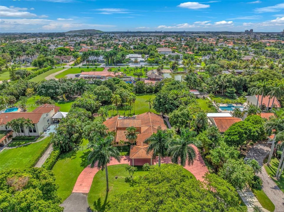 Expansive property featuring a red tile roof, mature palm trees, and a substantial driveway