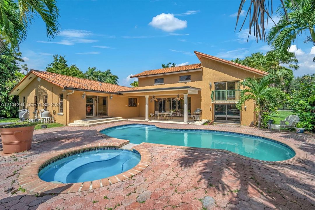 Mediterranean-style architecture featuring a tile roof, stucco exterior, a large in-ground swimming pool, an integrated spa, and an expansive paver patio