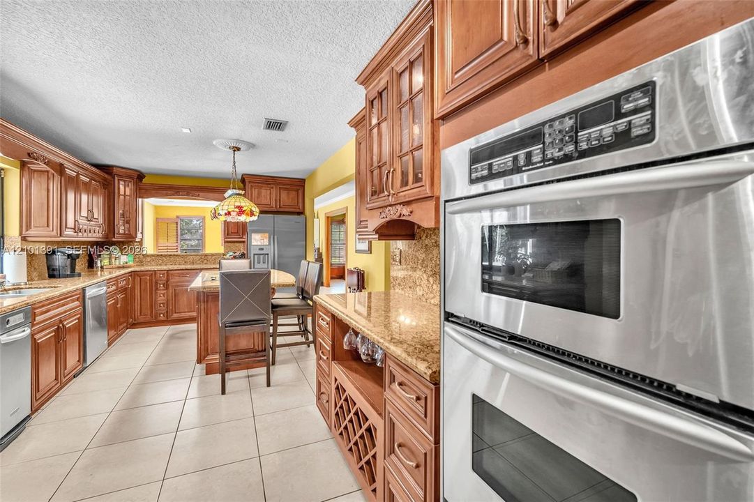 Kitchen featuring wood cabinetry, stainless steel double wall ovens, granite countertops, and tile flooring