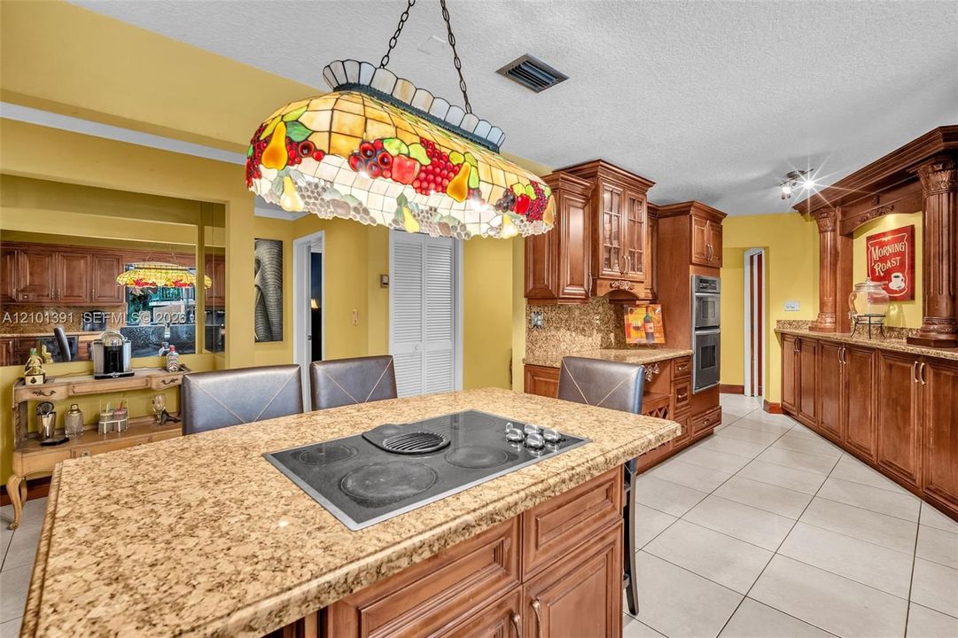 Kitchen featuring wood cabinetry, built-in double ovens, tile flooring, granite countertops, and a center island with an integrated cooktop