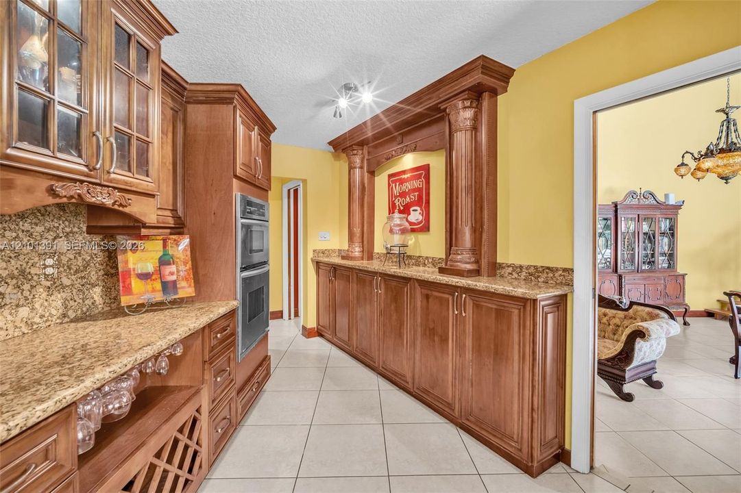 Kitchen featuring extensive wood cabinetry, granite countertops, built-in double ovens, a wine rack, and tile flooring